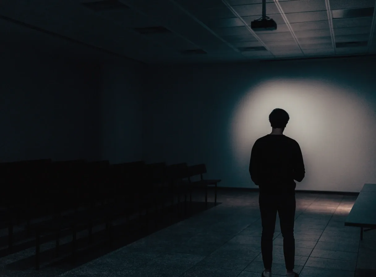 A person standing in front of an out-of-focus projection glow in a dark meeting room